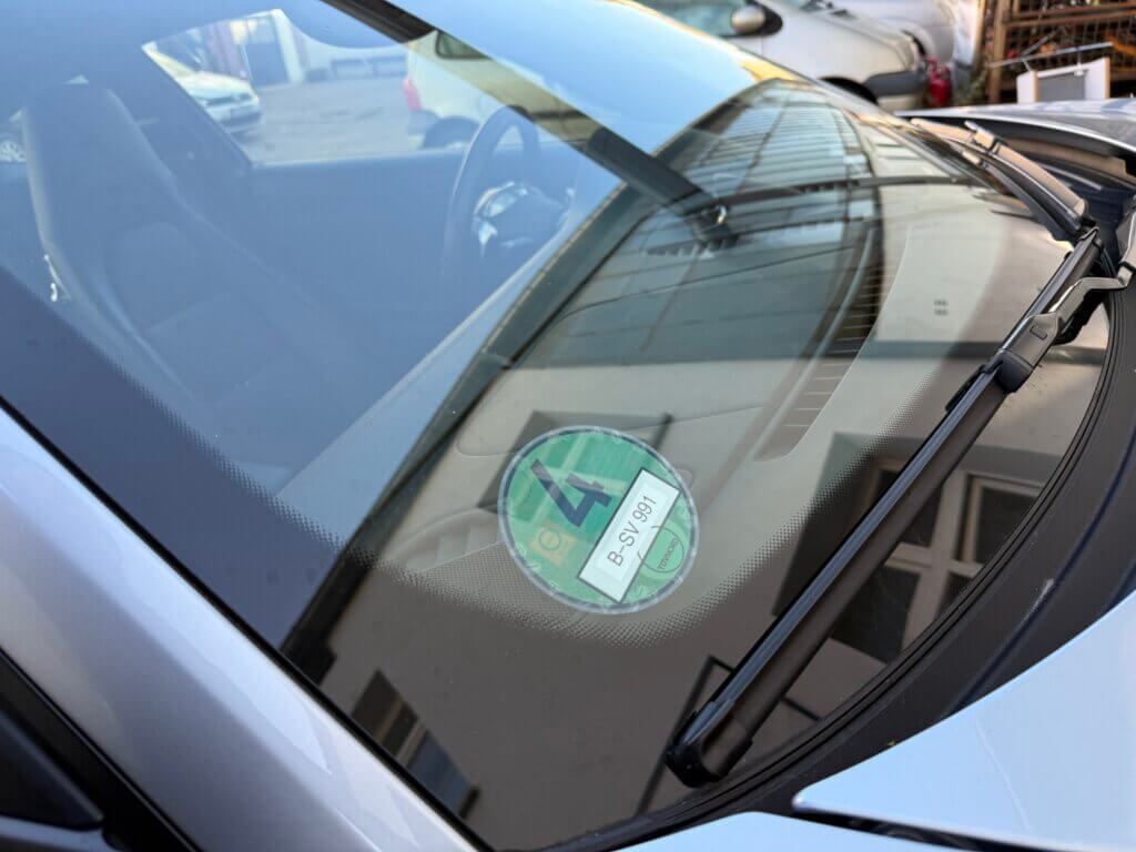 Frontscheibe eines Autos mit einer runden grünen Umweltplakette unten rechts auf der Beifahrerseite.